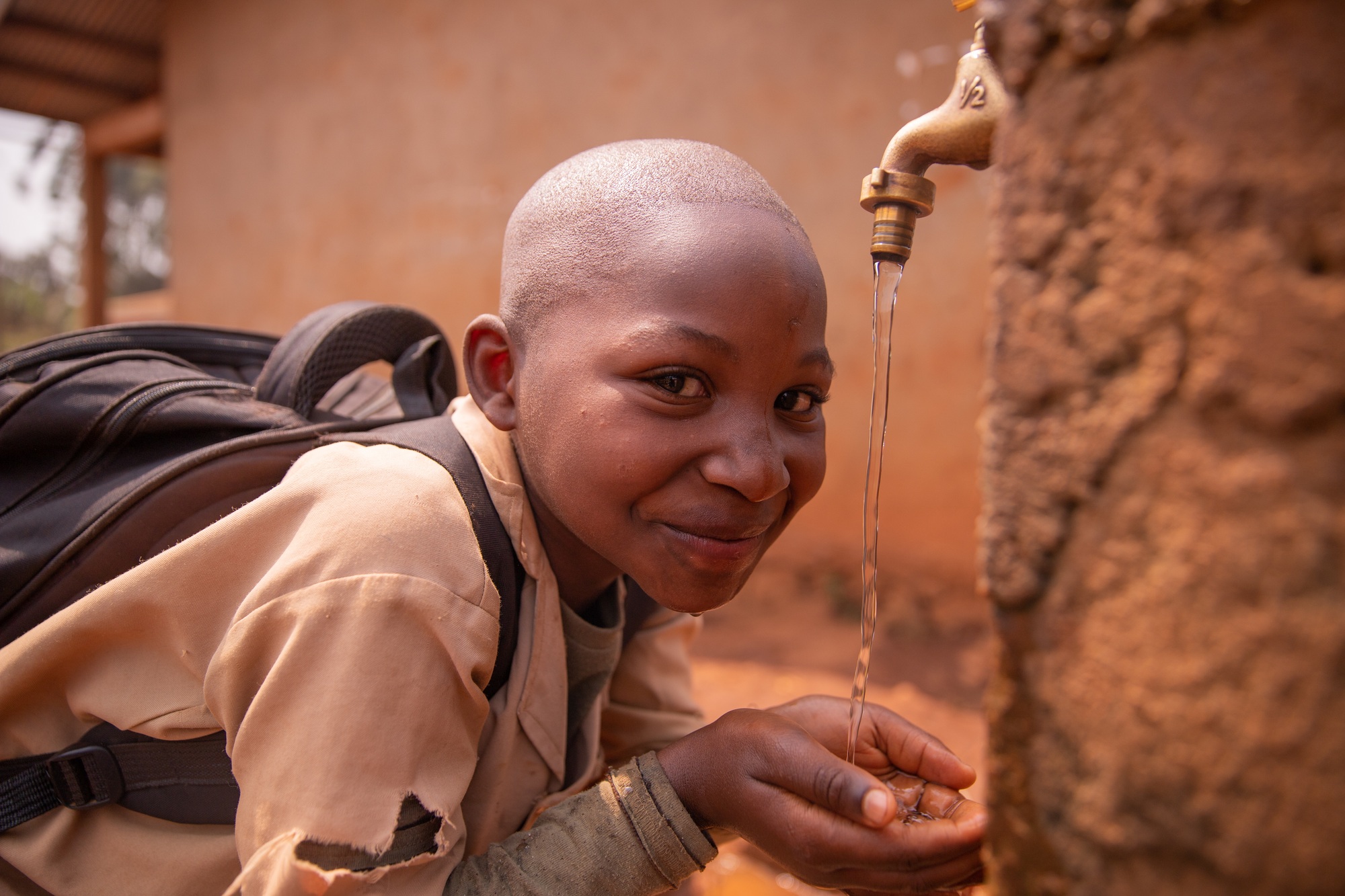 Black schoolchild collects water with his hands from the tap located in the schoolyard Water concept